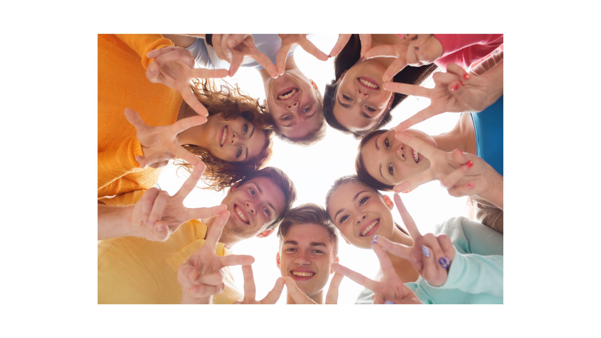 Zdjęcie przedstawia młody ludzi w okręgu pochylających się nad obiektywem aparatu