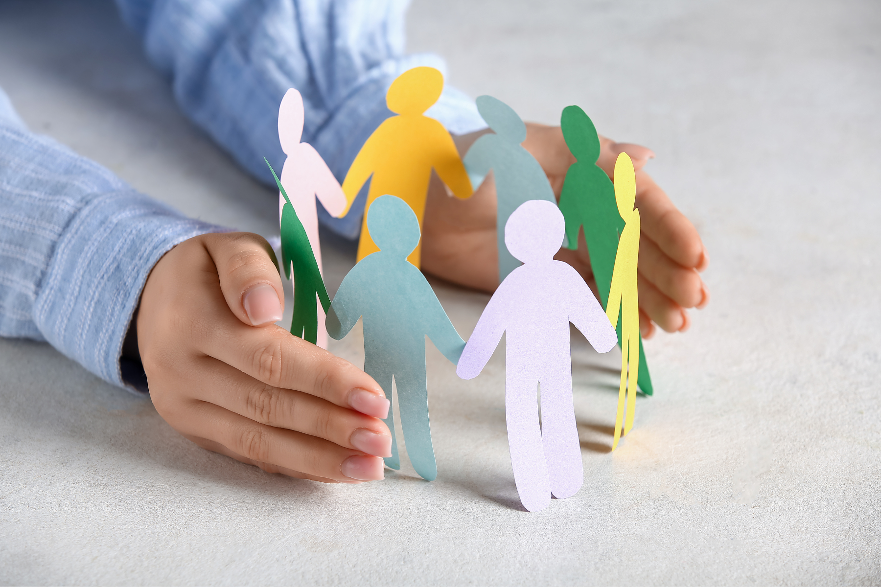 Ludzkie dłonie obejmują krąg papierowych figurek trzymających się za ręce