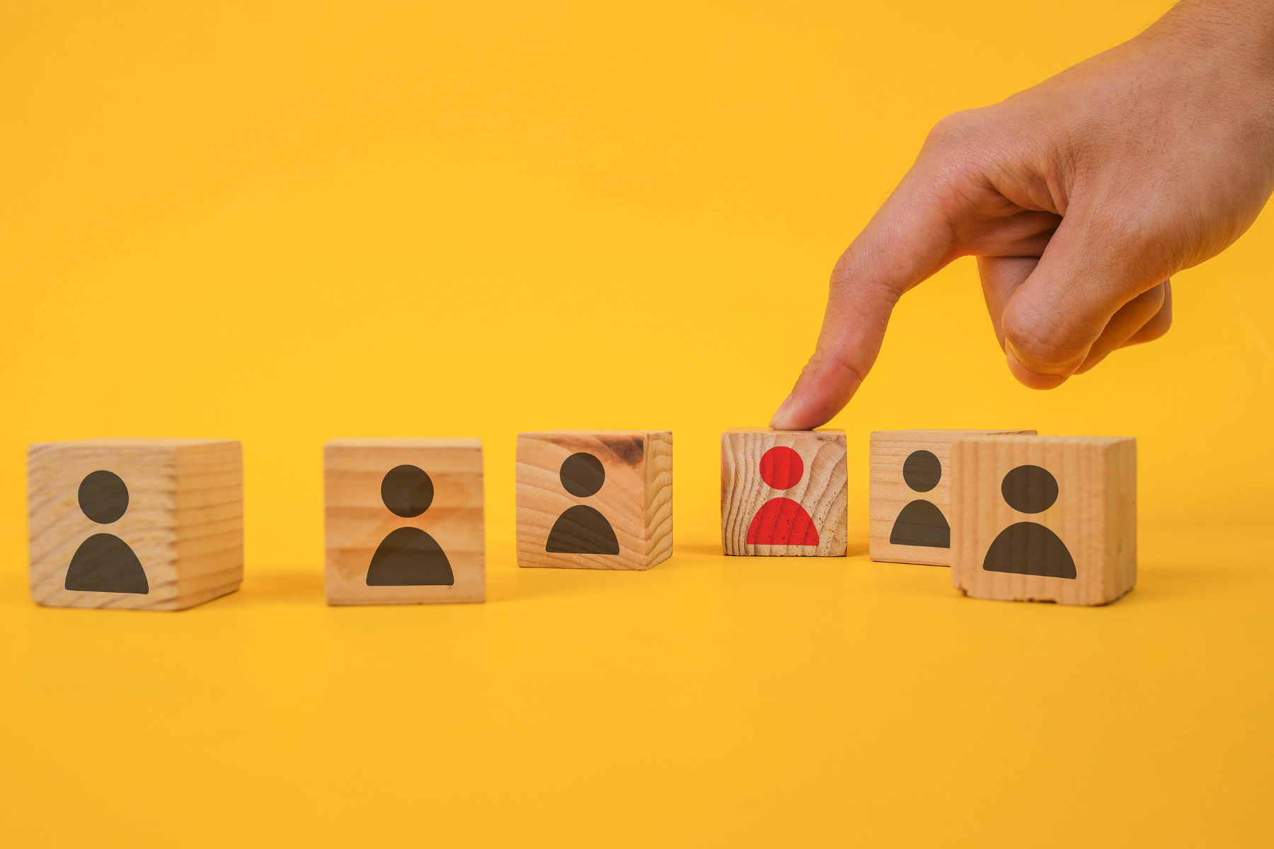 Ilustracja z drewnianymi kostkami oznaczającymi uczestników. Jeden wyróżnia się kolorem czerwonym