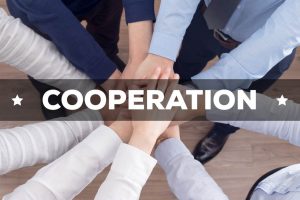 Splecione dłonie kilku osób z umieszczonym centralnie napisem: cooperation
